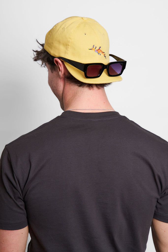 Female model wearing a Charcoal t-shirt and a faded yellow cap with a weedy seadragon design