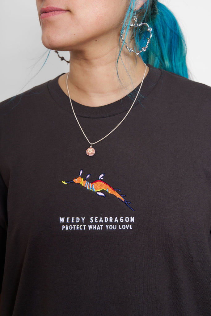 Female model wearing a Charcoal t-shirt with a weedy seadragon design and the Protect What You Love text.